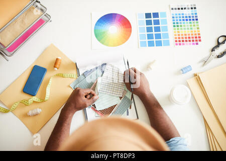 Overview of fashion designer hands over table with fabric samples, color swatches and other supplies during working process Stock Photo