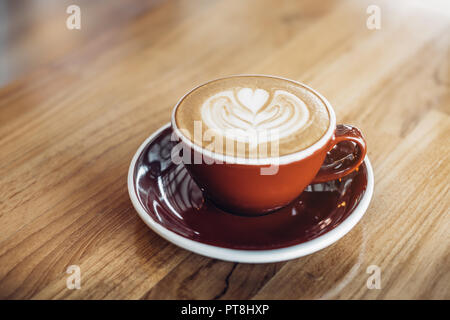 Close up hot cappuccino red coffee cup with heart shape latte art on wood table at cafe,Drak tone filter,food and drink Stock Photo