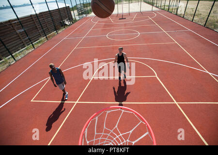 Full length high angle view portrait of two young men playing basketball in outdoor court lit by sunlight, copy space Stock Photo
