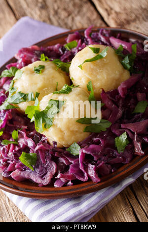 German food knodel potato dumplings and stewed red cabbage close-up on a plate on the table. vertical Stock Photo