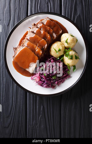 Festive German full dinner Sauerbraten - beef stew with gravy served with potato dumplings and red cabbage close-up on a plate. Vertical top view from Stock Photo