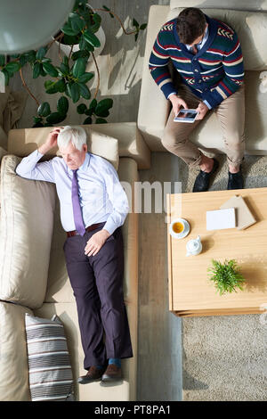 High angle view of serious senior businessman in shirt and tie lying on sofa and sharing his problems with psychiatrist who making notes in tablet at  Stock Photo