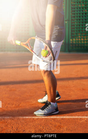 A tennis player prepares to serve a tennis ball during a match with sunlight in background Stock Photo