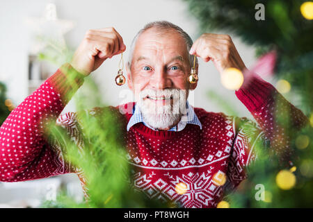 A senior man standing by Christmas tree, holding balls ornaments. Stock Photo