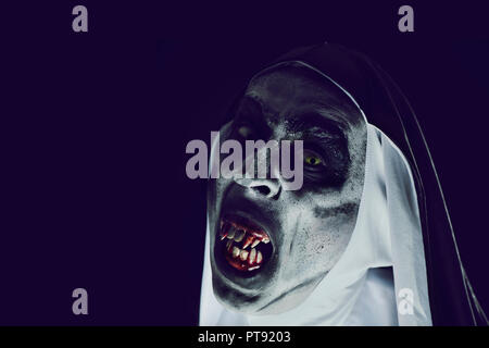 closeup of a frightening evil nun, with bloody teeth and scary eyes, wearing a typical black and white habit, against a black background, with some bl Stock Photo