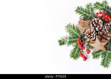 Christmas festive styled floral composition. Pine cones, fir tree branches, red rowan berries and wooden stars on white table background. Decorative frame, web banner. Flat lay, top view. Copy space. Stock Photo