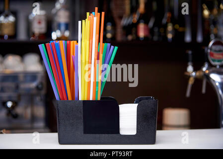 Multicolored straws with napkins stand on the bar counter. Stock Photo