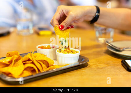 Womans hand with red color nail having a tortilla chip with nacho cheese sauce at lunch time Stock Photo