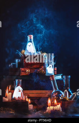 Little ghosts in glass jars. Halloween concept on a dark background with a stack of magical books and mysterious smoke. Stock Photo