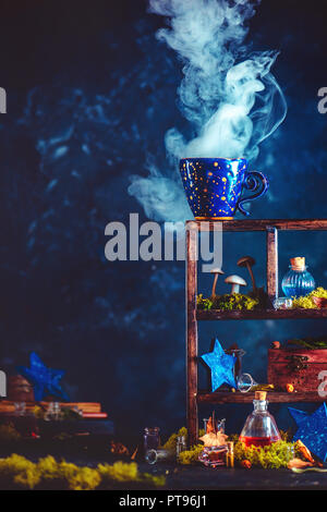 Ceramic cup with constellations and rising steam on a shadow case with mushrooms and crystals. Witch or wizard workplace with copy space. Stock Photo
