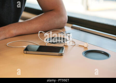 Close-up of headphones and cell phone lying next to a man on the table in the train during the trip. Stock Photo