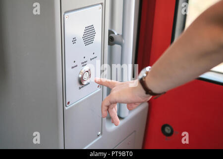 The person presses the button to call and talk with the support service of the train or subway. The inscription in German is translated as Call station - Operation - Service - Listen - Speak. Stock Photo