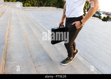 Cropped image of young business man with briefcase walking on stairs while holding arm in pocket Stock Photo