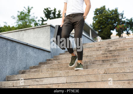 Cropped image of young business man with briefcase walking on stairs with arm in pocket Stock Photo