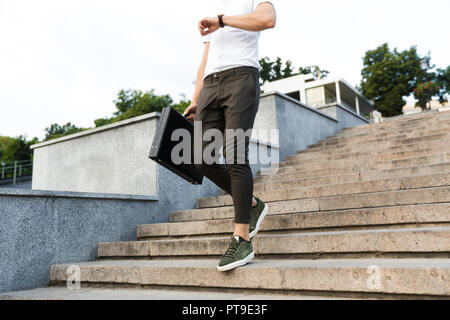 Cropped image of business man with briefcase looking at wrsistwatch while walking on stairs outdoors Stock Photo