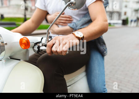 Cropped image of young lovely couple riding togother on the retro scooter outdoors Stock Photo