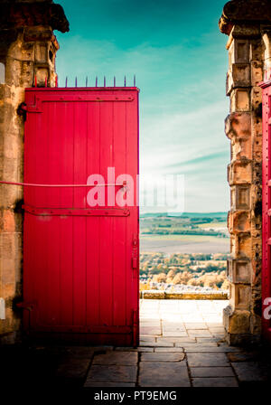 A large bright red door against a blue sky overlooking a long vista on a sunny autumn day. Stock Photo