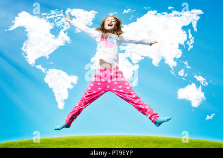 Happy girl jumping high on a green grass against clouds in shape of world map during sunny day. Stock Photo