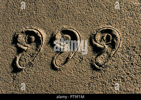 The numbers 999 cut into wet sand. Stock Photo