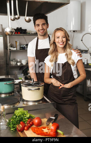 Image of happy young friends loving couple chefs on the kitchen cooking posing looking camera. Stock Photo