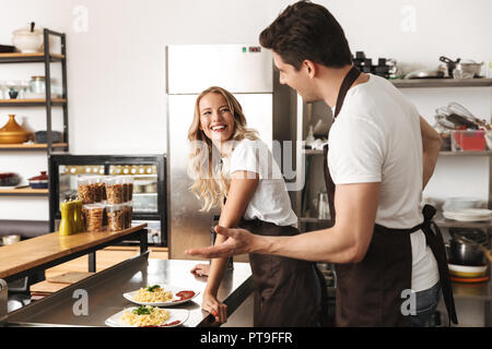 Smiling chefs couple dressed in aprons cooking together at the kitchen, talking Stock Photo