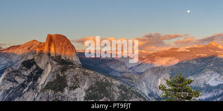 A Panoramic view of Half Dome and Yosemite Valley. Golden light from the sunset is cast upon the Mountain tops, while the moon is out. Image from Glac Stock Photo