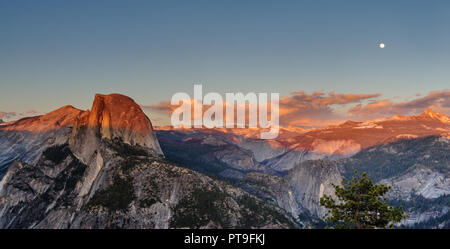 A Panoramic view of Half Dome and Yosemite Valley. Golden light from the sunset is cast upon the Mountain tops, while the moon is out. Image from Glac Stock Photo