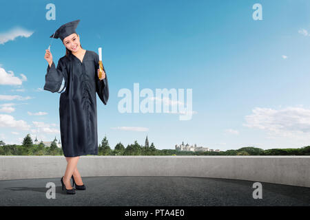 Smiling asian girl in graduation gown and hat standing at outdoor Stock Photo