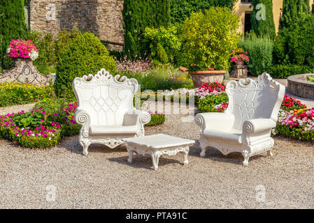 Horizontal photo of summer scene in Garzoni garden in Tuscany with big white plastic armchairs. The chairs are place on gravel with several colorful f Stock Photo