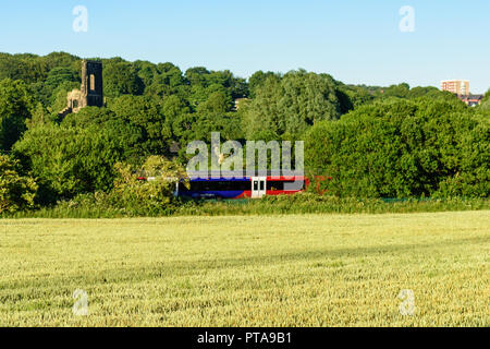 Leeds, England, UK - June 30, 2015: A Northern Rail Class 333 electric passenger train on the Airedale Line passes the ruins of Kirkstall Abbey, part  Stock Photo