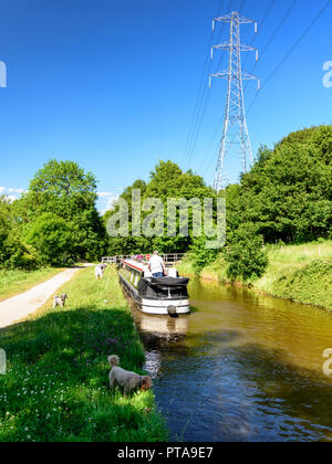 Shipley, England - June 30, 2015: A traditional narrowboat travels along the Leeds and Liverpool Canal on a sunny summer day, while wakers and dogs pa Stock Photo