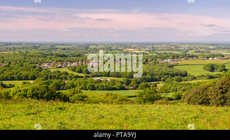 Sun shines on the village of Pett and a patchwork of woodland and farm fields in East Sussex as viewed from the high vantage point of Fairlight hill. Stock Photo