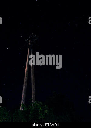 electricity post standing in the middle of the night light up by the stars Stock Photo