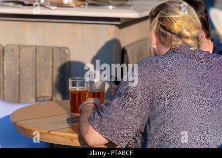 Two people sit at the table in the cafe, talk and drink beer. View from the back. Stock Photo