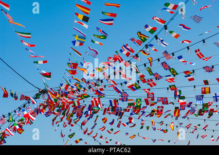 World flags in the form of bunting on multiple lines leading to a central pint against a clear blue sky Stock Photo