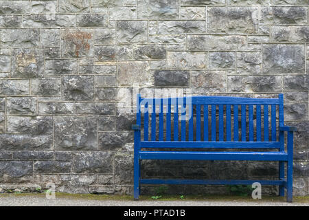 Old blue wooden bench against a grey gray stonewall. Relaxing spot to sit and contemplate Stock Photo