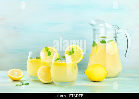 A side view of homemade lemonade in glasses and a pitcher, with fresh lemons and mint, on a teal background with copy space Stock Photo