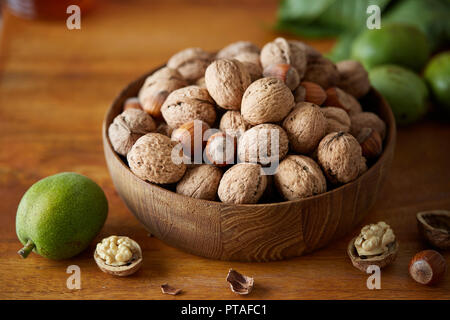 Bowl of walnuts and hazelnuts on wooden table. Fresh walnuts with and without shells on a wooden surface. Stock Photo