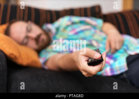 Man relaxing in sofa with remote control watching tv. Shallow dof focus on remote control. Stock Photo