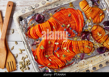 sliced pumpkin baked in an oven on a rustic baking tray with onion, dried lavender and spices, view from above, flat lay, close-up Stock Photo