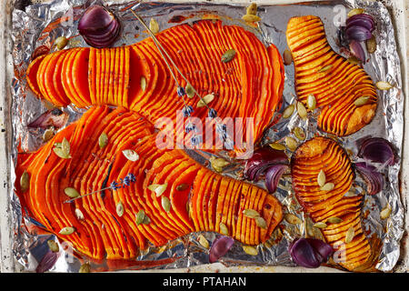 close-up of sliced pumpkins baked in an oven on a rustic baking tray with onion, dried lavender and spices, view from above, flat lay Stock Photo