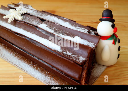 Buche de Noel or Chocolate Yule Log Cake for Christmas Celebration with a Cute Snowman Marzipan on a Wooden Table Stock Photo