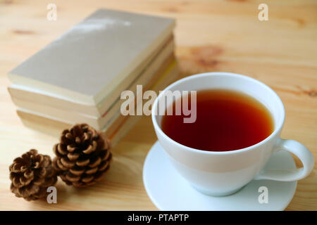 Closed up a cup of hot tea with dry pine cones and stack of books on natural color wooden table Stock Photo