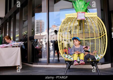 Children sitting and lounging in a big pineapple chair, Cotters market on Flinders Street, central business district of Townsville City QLD, Australia Stock Photo