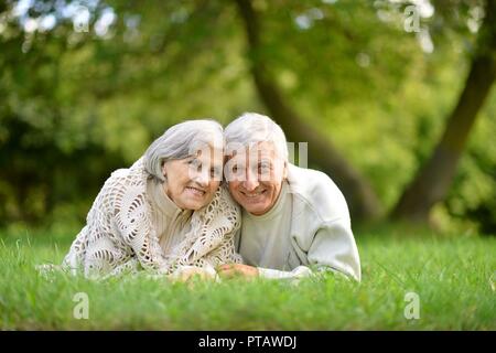 Portrait of elderly couple lying on green grass in summer park Stock Photo