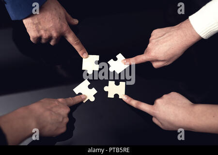 Closeup of business people wanting to put four pieces of puzzle. Stock Photo
