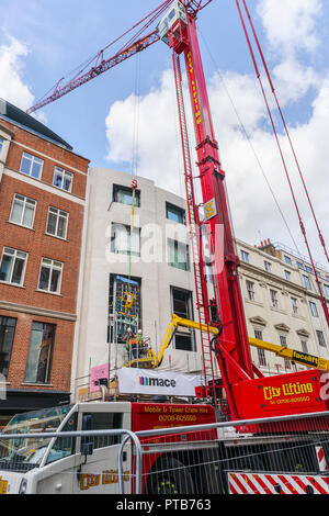 Building contractor Mace workers on a cherry picker hoist carefully fitting a large new glass window pane into a building in Mayfair, London, UK Stock Photo