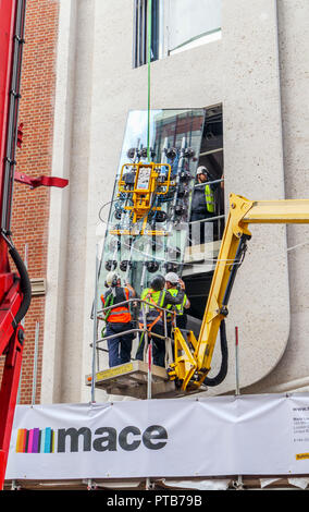 Building contractor Mace workers on a cherry picker hoist carefully fitting a large new glass window pane into a building in Mayfair, London, UK Stock Photo