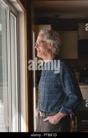 Senior man looking through window at home Stock Photo