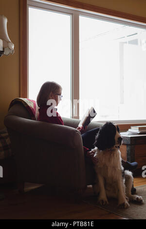 Senior woman reading book while dog sitting beside her Stock Photo